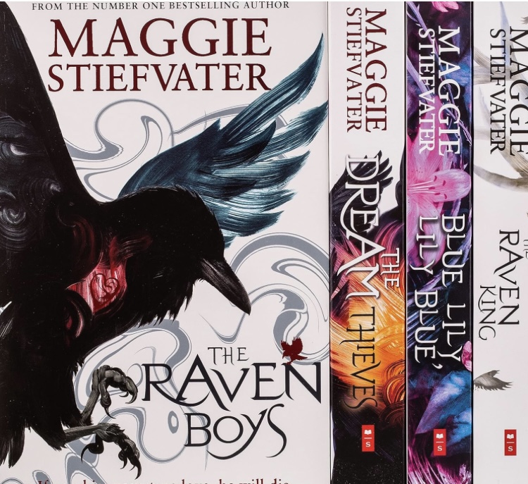 Book cover text: Maggie Stiefvater, The Raven Boys
Image: Artistic rendering of a raven on a white cover. The spines of three other books in the photo read: The Dream Thieves, Blue Lily Lily Blue, Raven King